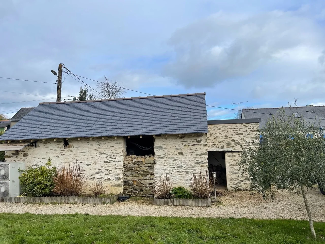 Couverture en ardoise posée sur un bâtiment en pierre, vue depuis le jardin.