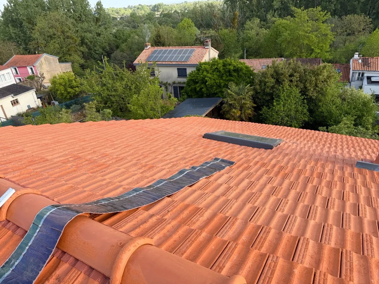 Couverture en tuiles orangées avec une fenêtre de toit et une bande de closoir visible au faîtage.